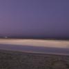 Mark and Kate sit on the beach at night.  The distant white light is the Cape Lookout lighthouse